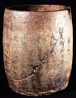 全体が茶褐色で光沢があり、表面にびっしりと文字が彫られている陶製経筒の写真