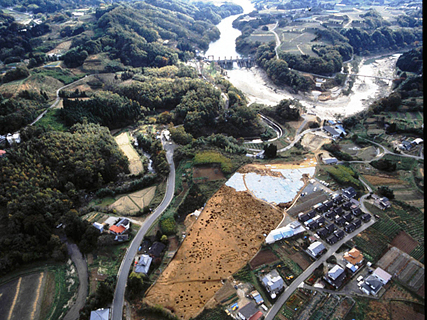 周りに山や川などがあり、広い土地に所々丸い穴が開いている地面が見える和台遺跡を上空から撮影した写真
