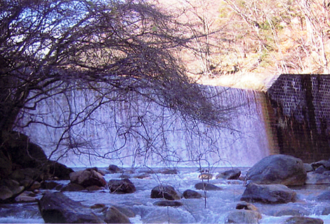 大きな石などが所々ある川の奥に見える荒川第七堰堤の写真