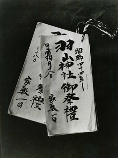 筆で文字が書かれた長方形の白い紙が、右上の角で紐で閉じられている金沢の羽山ごもり託宣記録の写真