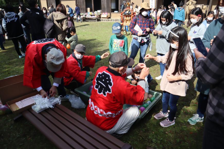 背中に「祭」と書かれた赤い法被を着た男性が女の子にヨーヨーを渡そうとしている様子の写真