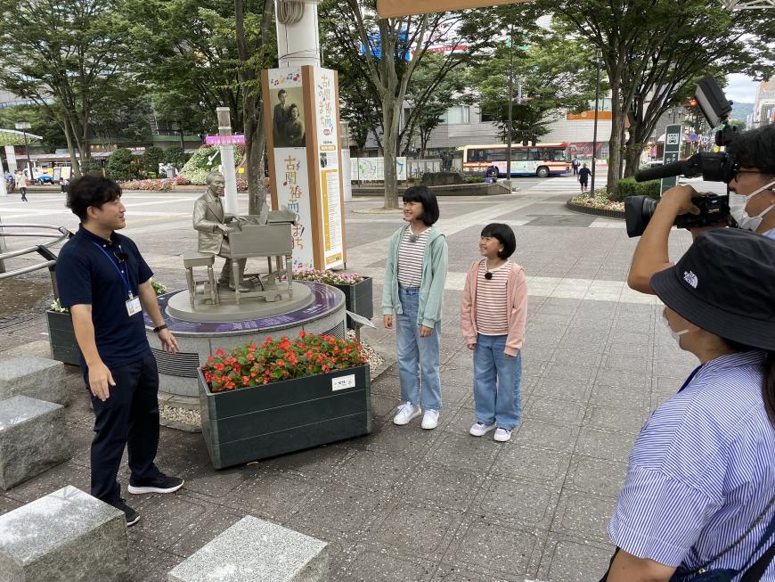 古関裕而氏のモニュメントが設置されている広場でロケを行っているまーちゃんおーちゃんの写真