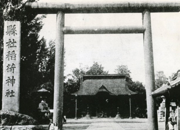 鳥居横に「縣社稲荷神社」と書かれた石碑が建てられた稲荷神社の外観を撮影した白黒写真