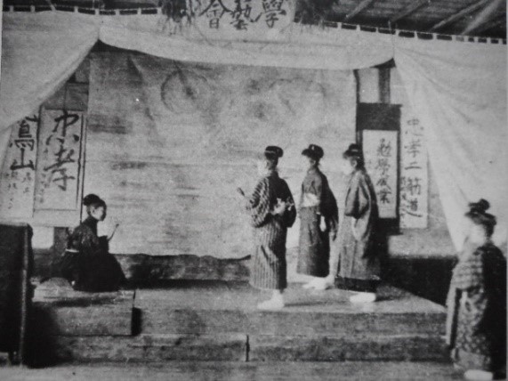 白い幕が掛けられた舞台上で、着物姿で烏帽子をかぶった4名の児童が劇を披露している学芸会の様子を写した白黒写真