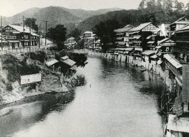 遠くには山並みが見え、小舟が停泊している摺上川の両岸に旅館が立ち並ぶ大正時代の飯坂温泉の風景の白黒写真