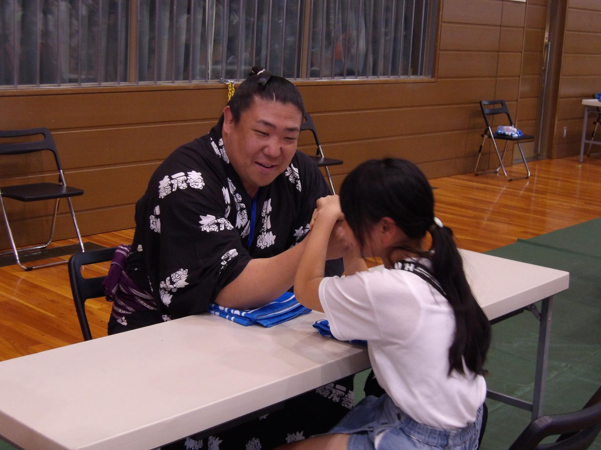 両手を使っている女の子と力士が腕相撲をしている写真