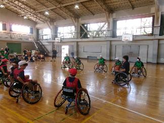 車いすに乗った豊島氏がボールを手にもってこれから試合をする子どもたちに説明している写真