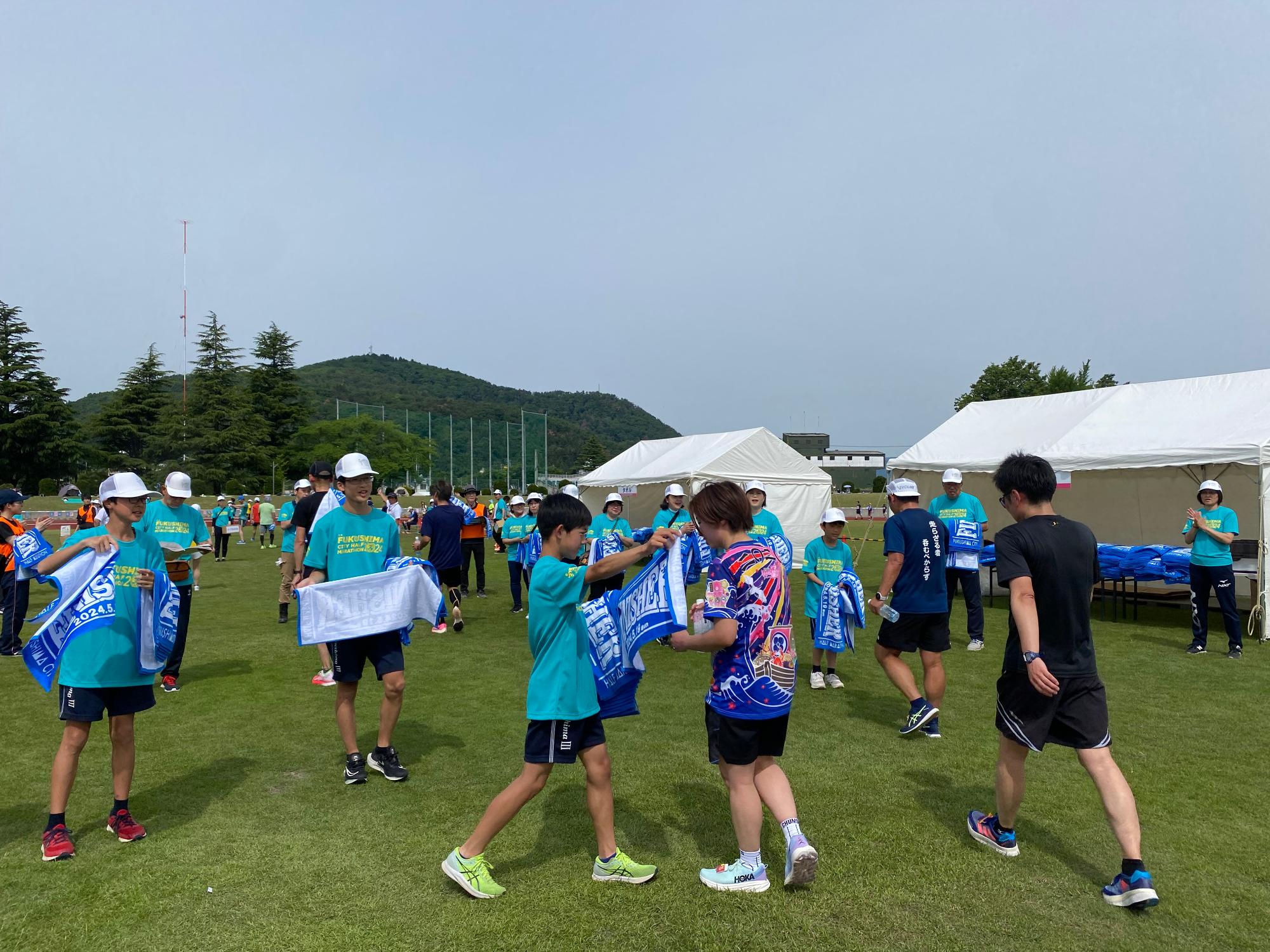 参加者にタオルを持って行っているエメラルドグリーンのシャツを着た関係者達の写真