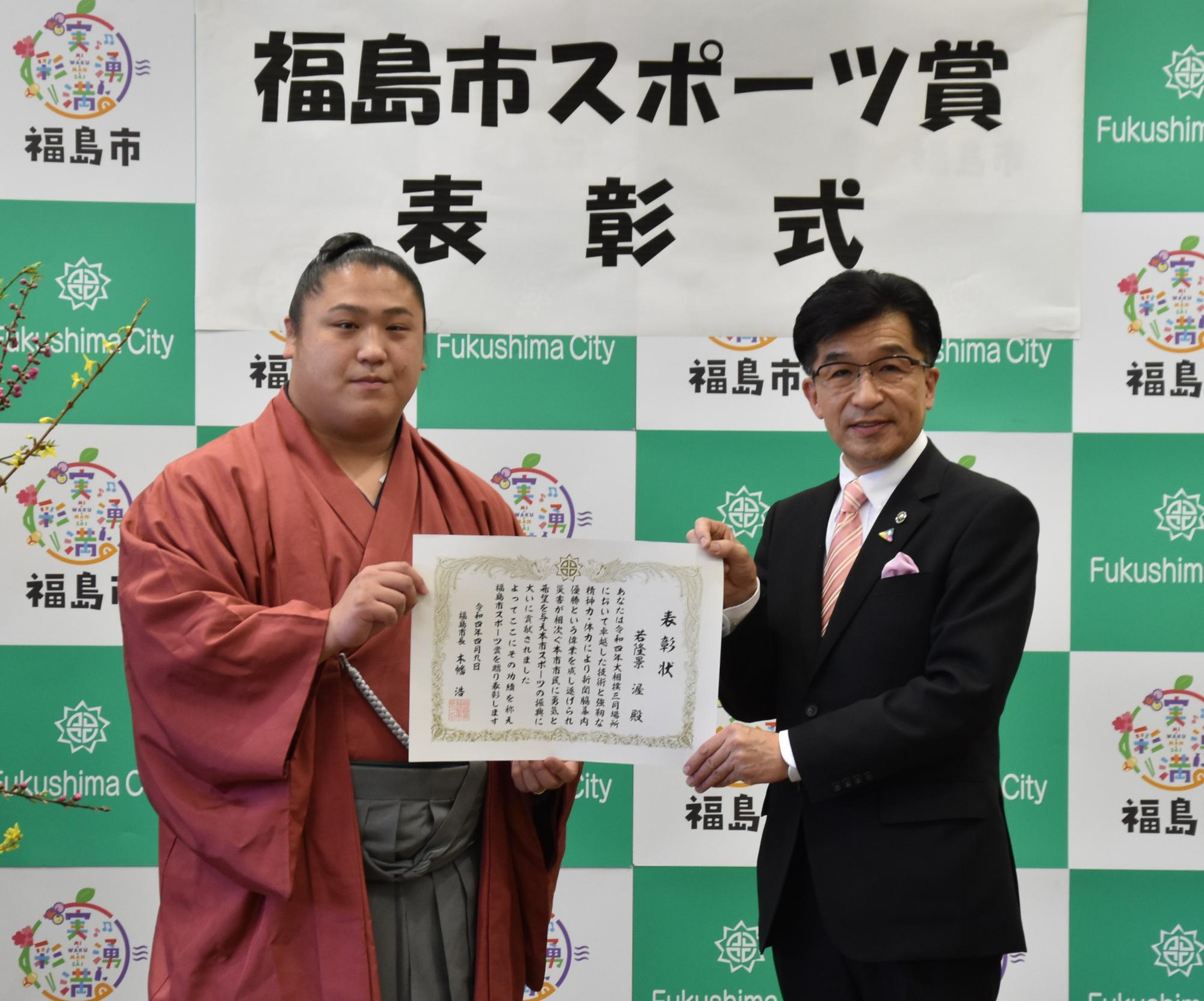 福島市のバックパネルの前で、「若隆景」関と木幡市長が一緒に賞状を持っている写真