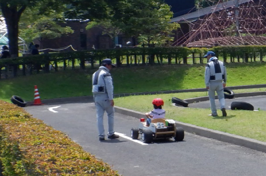電動カートに乗ってコースを走っている子供と見守るスタッフの写真