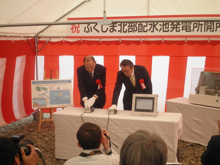 紅白の幕が張られたテントの中で機械のスイッチに手を置いている堀部慶次代表取締役社長と八島洋一福島市水道事業管理者の写真