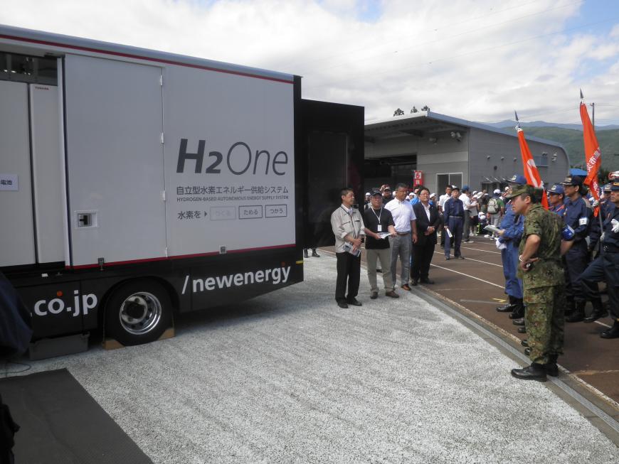 車体に「H2One」と書かれたトラックの周囲に集まった警察機動隊員や自衛隊員の写真