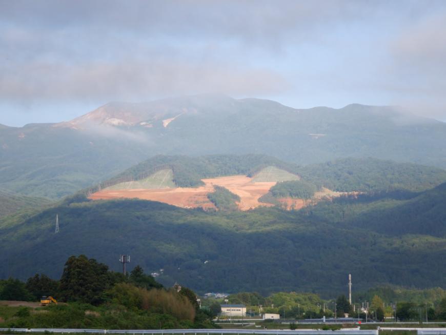 空に薄く雲がかかっており中央付近の山肌が見えている先達山の写真
