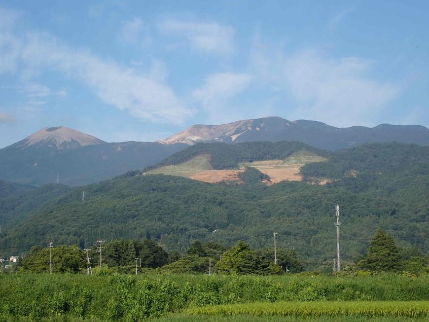 青空に薄く雲がかかっており、緑の草木が茂っているその奥に先達山が見えている写真
