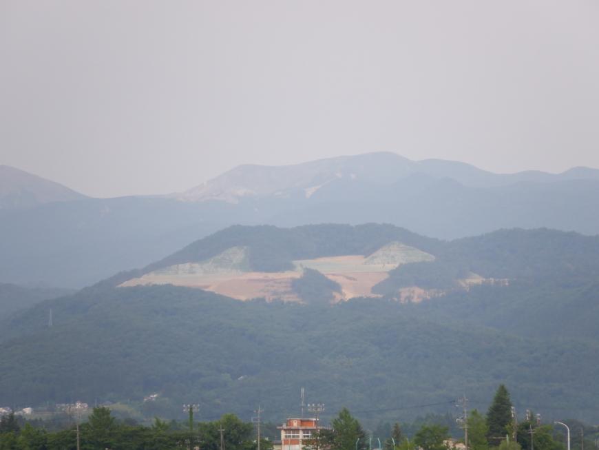曇り空で薄暗い中、中央付近の山肌が見えている先達山が写っている写真
