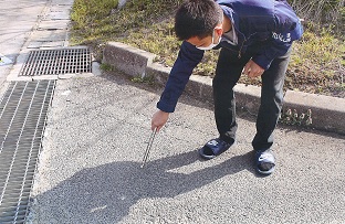 マスク姿の男性が道路に落ちているゴミを火ばさみで拾っている写真