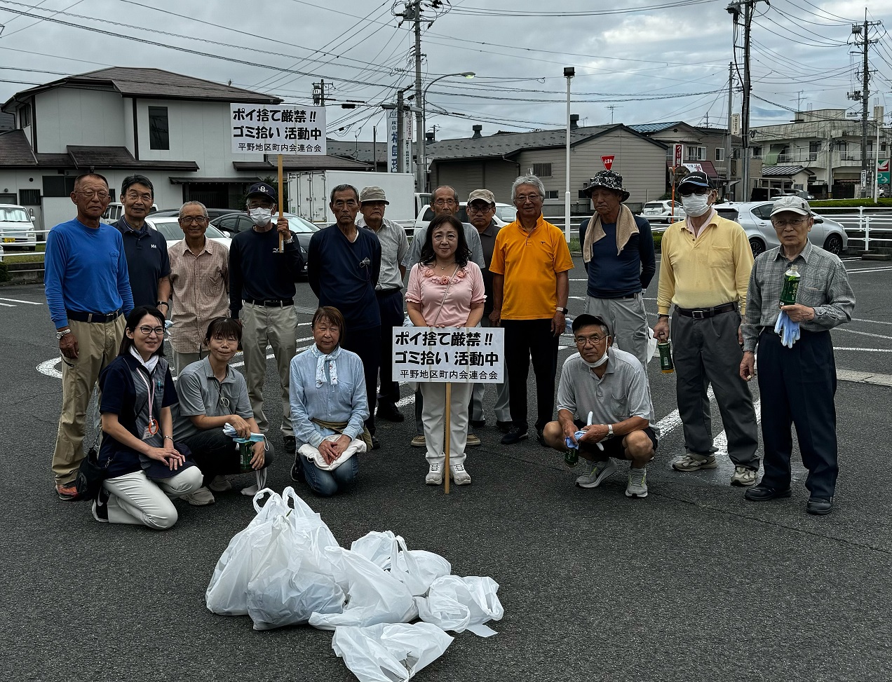 集めたゴミ袋を前に「ポイ捨て厳禁！！ゴミ拾い 活動中」と書かれたプラカードを持ち参加者の方々が記念撮影をしている写真