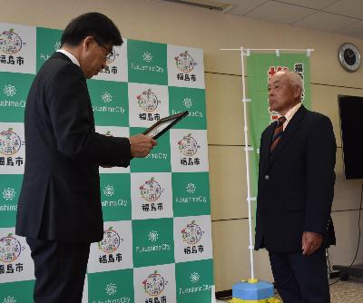 市長が指定書を読み上げている様子を各推進モデル地区の代表者の方が向き合って立っている写真