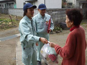 担当職員が住民の高齢女性から直接手渡しで家庭ごみを受け取っているふれあい訪問収集の様子の写真