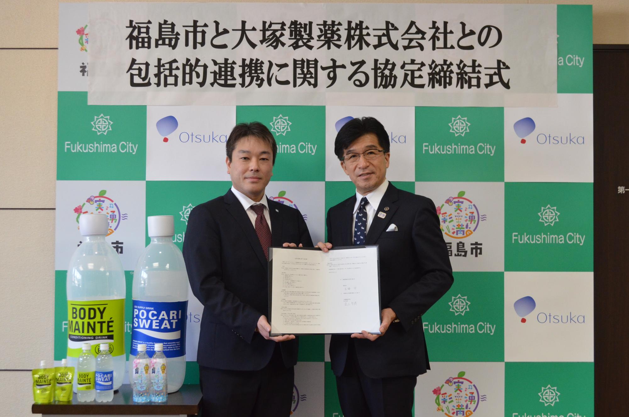 福島市と大塚製薬株式会社との包括的連携に関する協定締結式の幕の下で市長と支店長が協定書を持ち記念撮影をしている写真