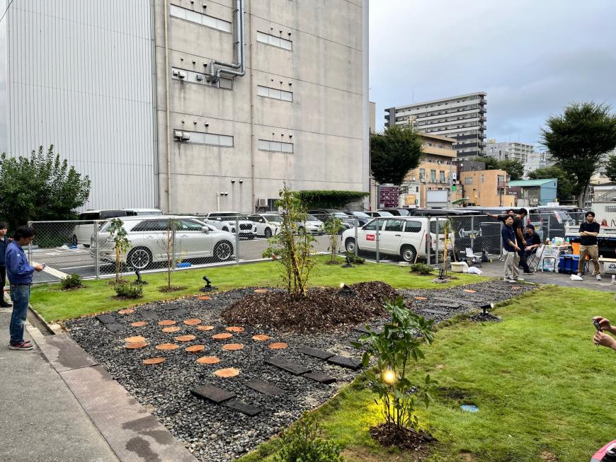 両脇が芝生で中央に石や木材などでデザインされた小道が造られ植物が所々に植えられている施工後の写真