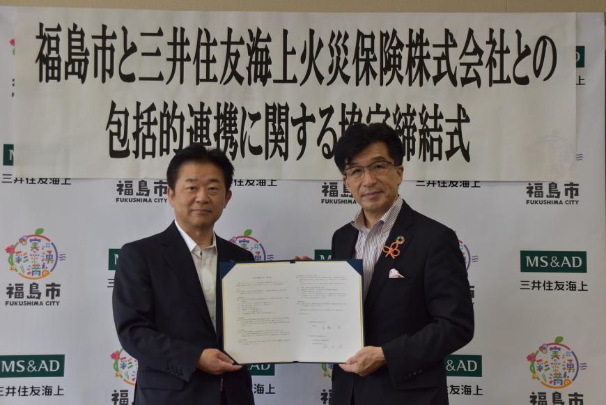「福島市と三井住友海上火災保険株式会社との包括的連携に関する協定締結式」の横断幕が掲げられたバックボードの前で、藏田東北本部長と木幡市長が並んで協定書を持ちながら記念撮影をしている写真