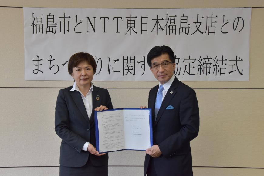 「福島市とNTT東日本福島支店とのまちづくりに関する協定締結式」と書かれた横断幕の前で、山貫支店長と木幡市長が協定書を両側から持ち記念撮影をしている写真