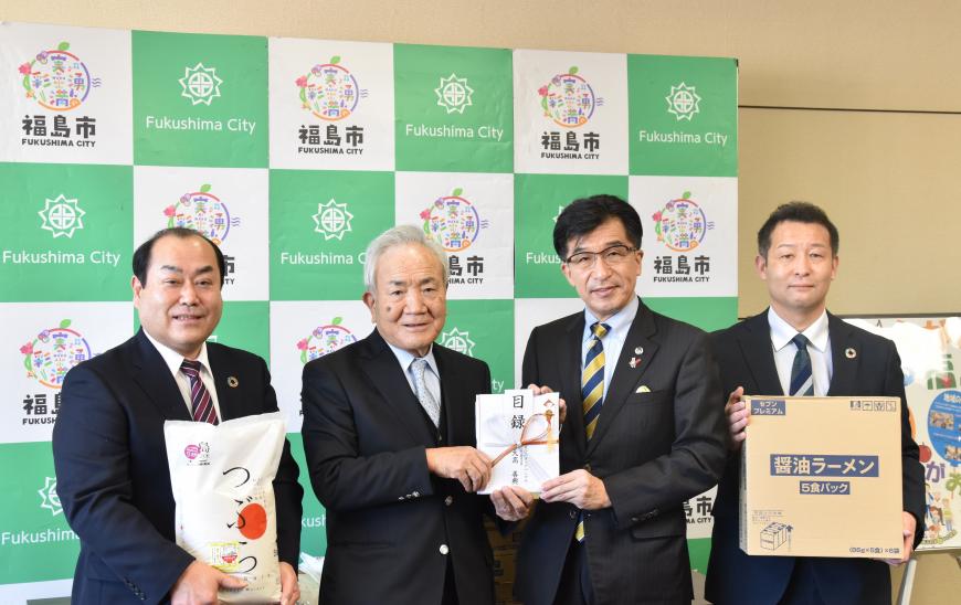 市長と大高会長が目録を持ち両脇の男性がお米とラーメンの箱を持ちながら記念撮影をしている写真