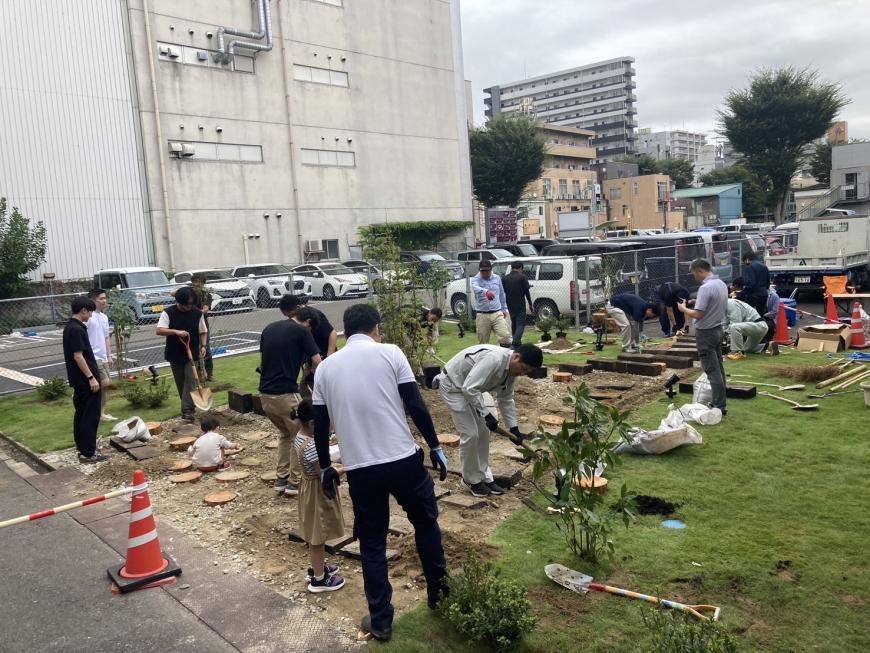 たくさんの関係者が土を掘り起こして石や木材などを置いている施工中の写真