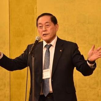 渡邊博美福島商工会議所会頭がマイクの前で両手を広げながら挨拶をしている様子の写真