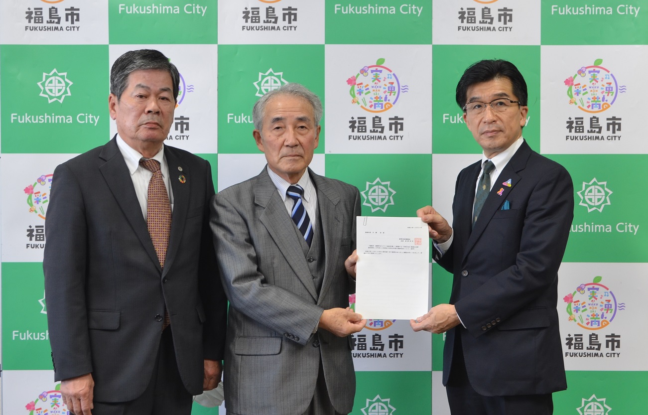 バックボードの前で市長と関係者の男性が両手で答申書を持ち3名で記念撮影をしている写真