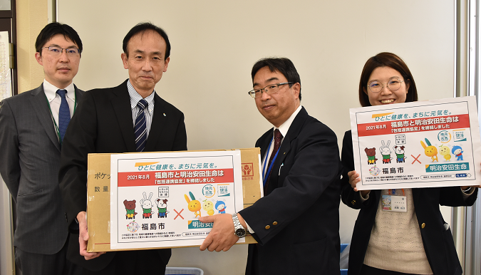寄贈する箱に入ったポケットティッシュやパネルを持った明治安田生命の関係者4名の写真