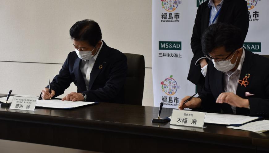 藏田東北本部長と木幡市長が並んで協定書に署名をしている写真
