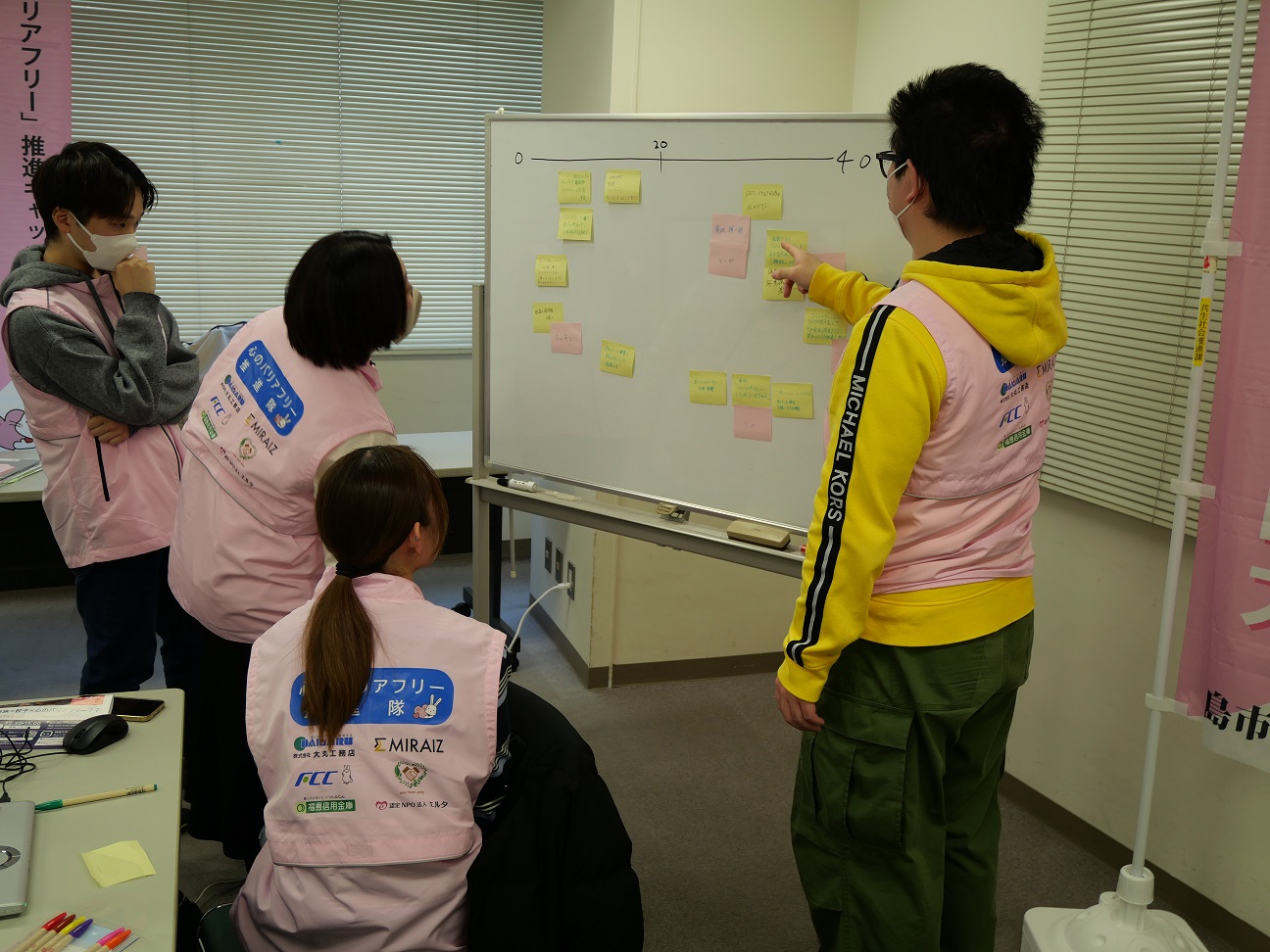 ホワイトボードを指さす隊員と立ち上がって覗き込む隊員一同