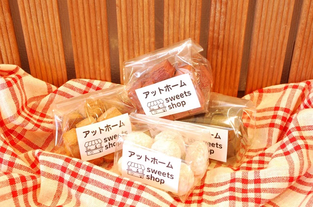 クロスの上に置かれた透明の袋に「アットホームsweets shop」と書かれたラベルが貼られた4種類の大豆クッキーの商品の写真