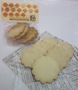 ベージュ色のラベルが貼られた透明袋に入ったお菓子の商品と、英語が書かれた紙の上に8枚のハニーレモンクッキーが並んでいる写真
