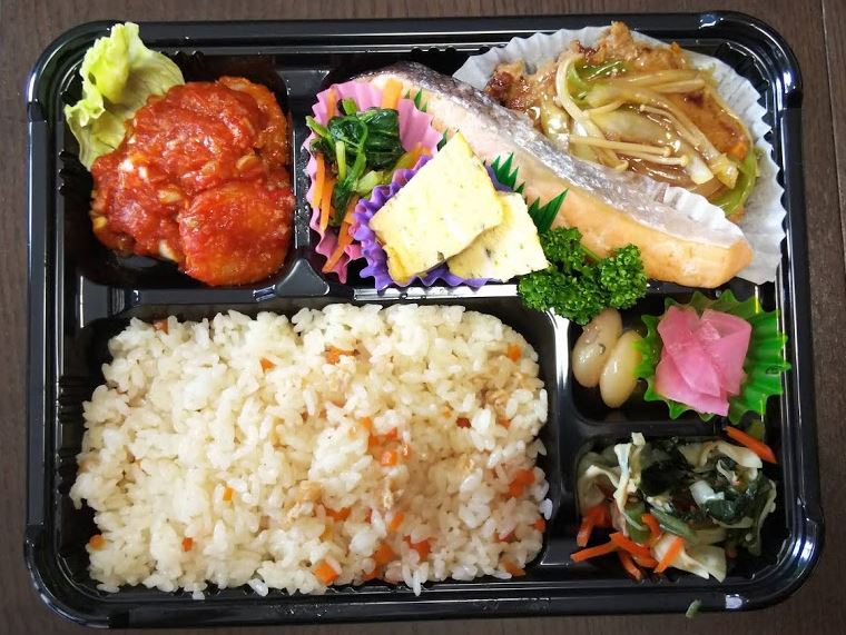 弁当容器に五目御飯やエビチリ、鮭や野菜のおかずが盛り付けられたお弁当の写真