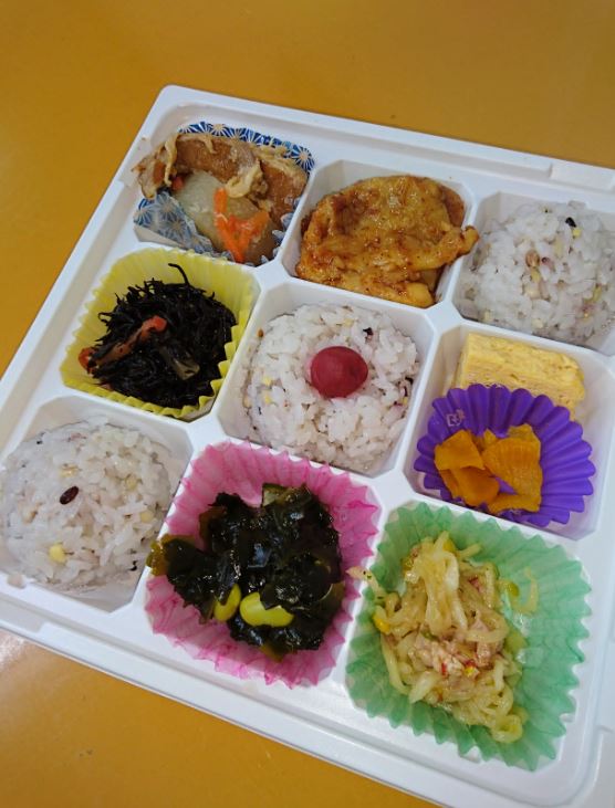9つのくぼみがある弁当容器に、ご飯や唐揚げ、沢山のおかずが盛り付けられた日替わり弁当の写真