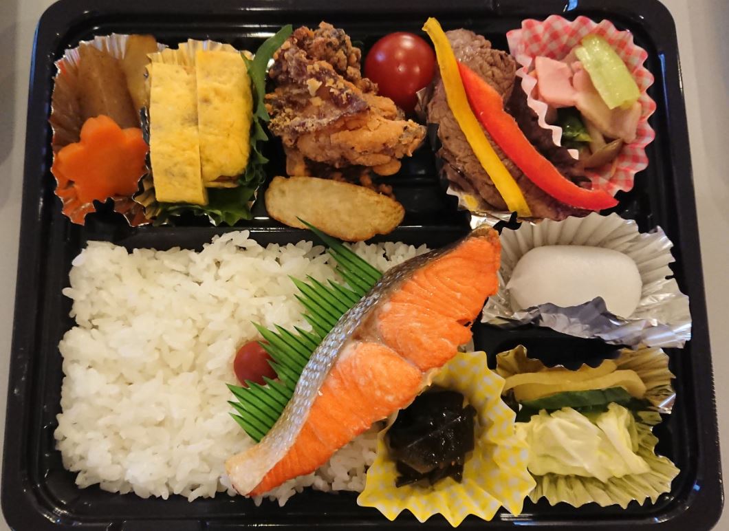 弁当容器に白ご飯、唐揚げ、煮物など沢山のおかずが盛り付けられたお弁当の写真