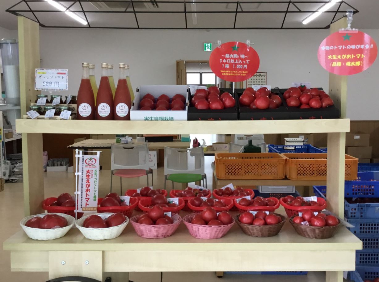 木製の2段の棚にカゴに入ったトマトや、瓶入りのトマトジュースなどが並んでいる直売所の写真
