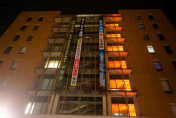 3枚の垂れ幕が掲示された福島市役所本庁舎の3階から9階までがオレンジ色にライトアップされている様子を下から撮影した写真