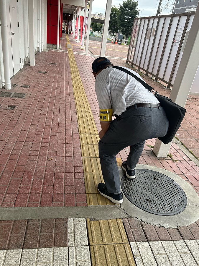 黄色の腕章をつけた男性が中腰になって煙草の吸殻を拾っている写真