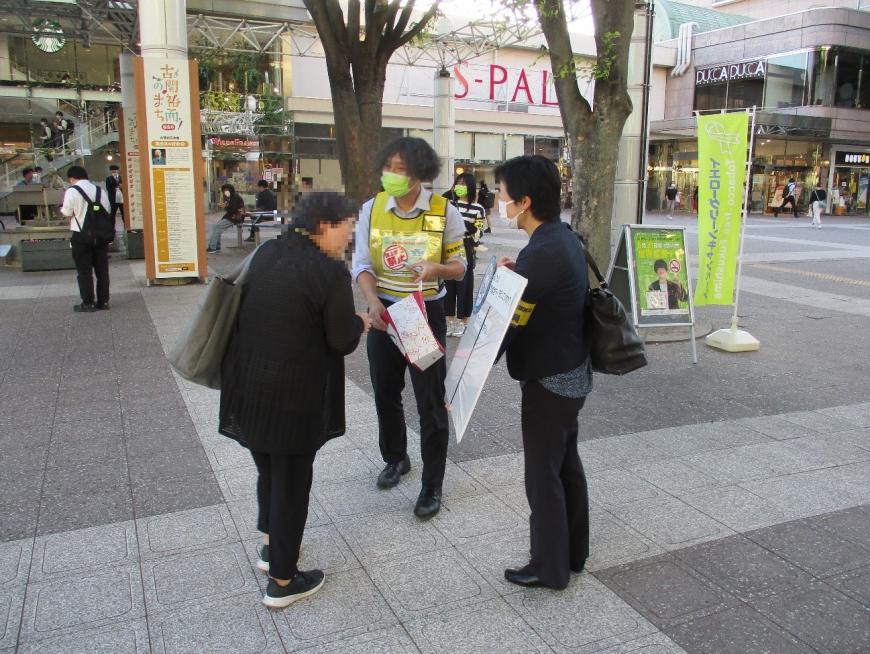 黄緑色ののぼりを立て、街頭で黄色のビブスを着た男性と、パネルを持った女性が周知・啓発活動をしている様子の写真