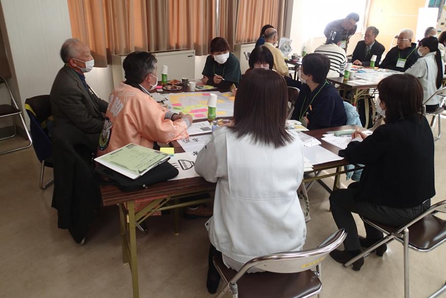 グループに分かれてテーブルの席に座った委員たちが付箋メモなどを使ってアイディアを出し合っている様子の写真