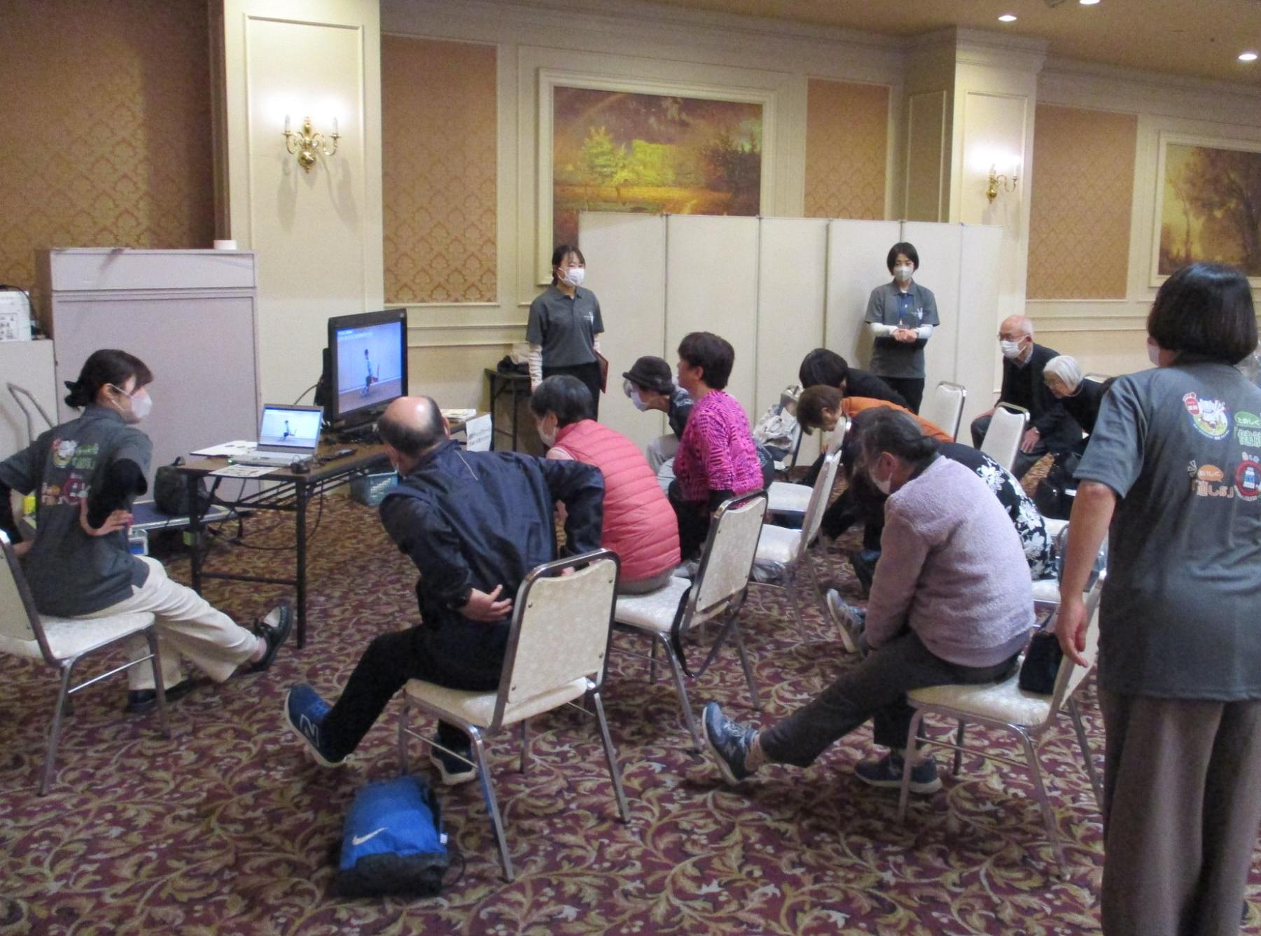 けんトレ体験コーナーで放映されている動画を見ながらけんトレを行う市民ら