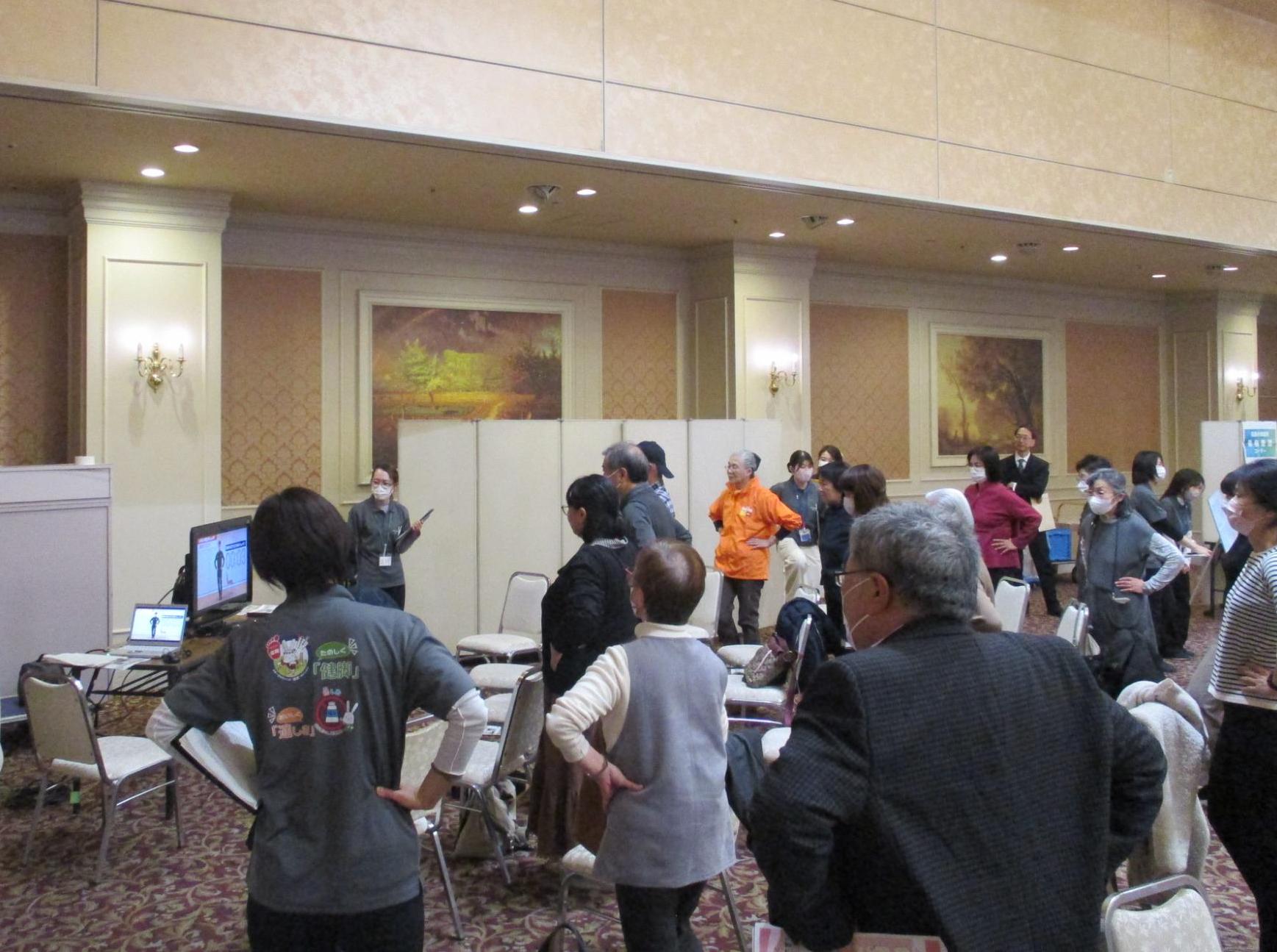 けんトレ体験コーナーで健トレの動画を見ながら実践する市民ら