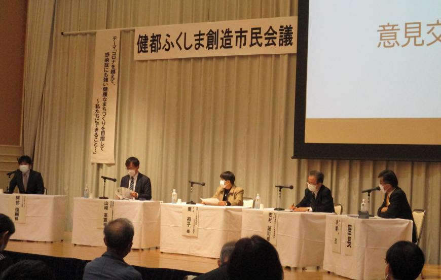 「健都ふくしま創造市民会議」の横断幕が掲げられたステージに設けられた席に5名の男女が座っている写真