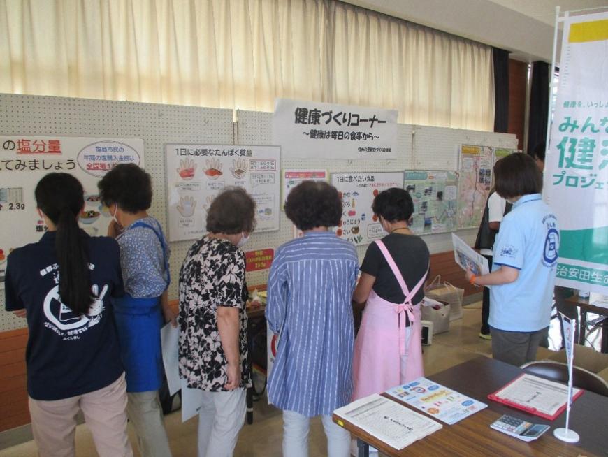 「健康づくりコーナー」とタイトルが貼られたパネル展示の前に6人の女性が集まり、展示を見ている写真