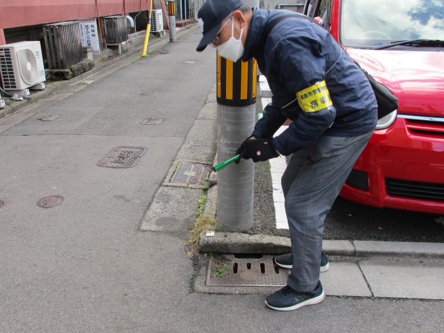 黄色の腕章をつけた男性が、火ばさみを持って腰をかがめてごみ拾いをしている写真