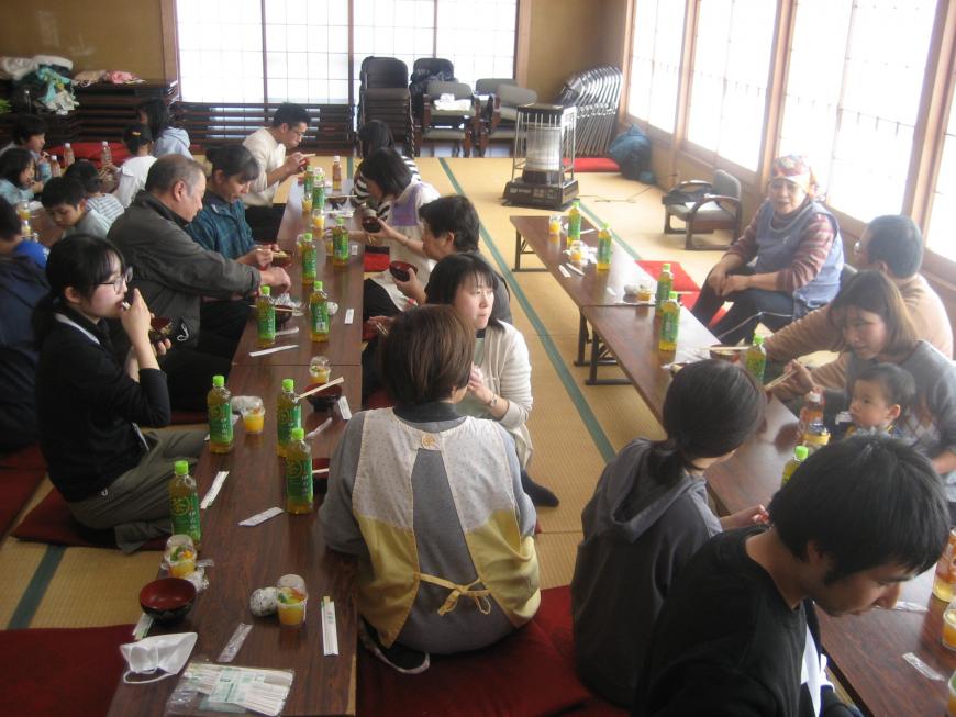座敷に2列並べた長机の両側に座った参加者たちが食事をしている様子の写真